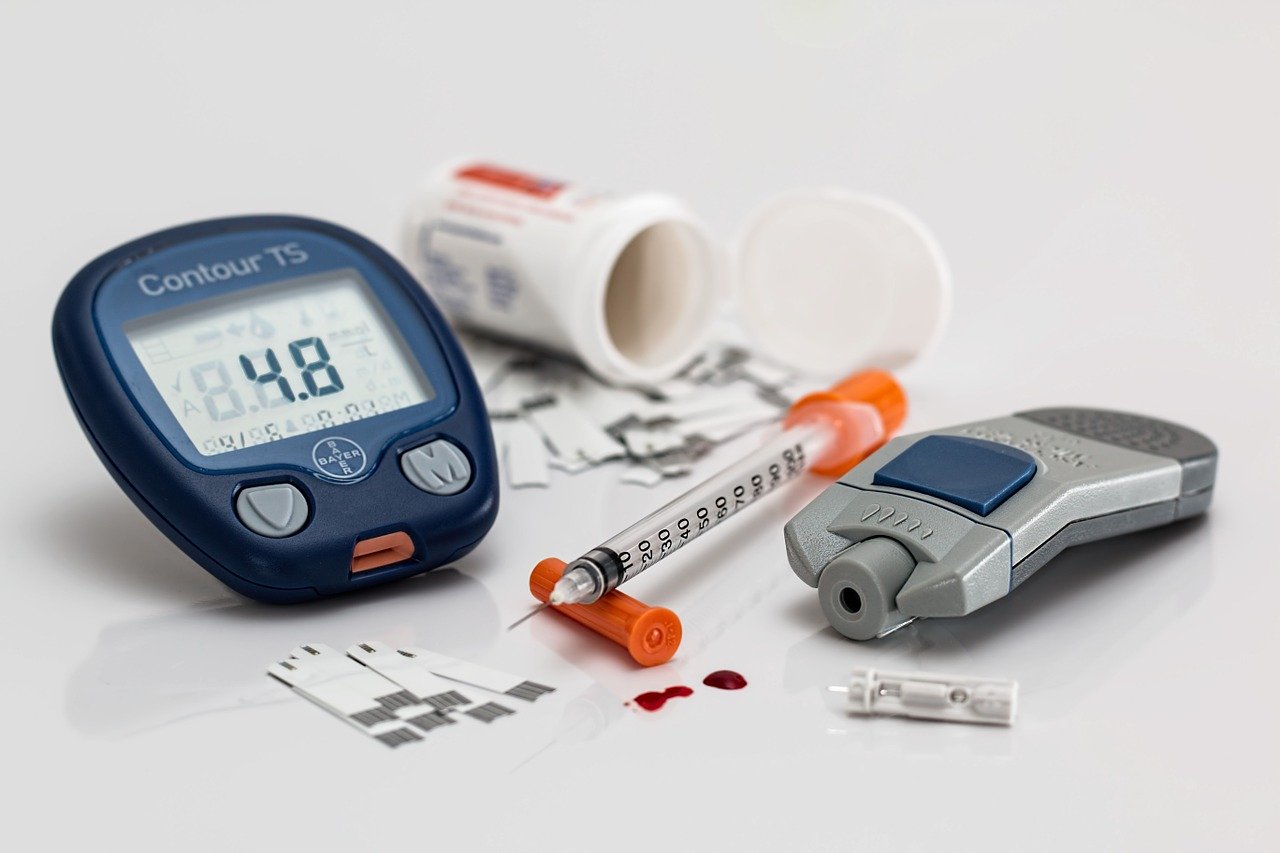 Various diabetes supplies on a table, including a monitor, test strips, and an insulin needle.